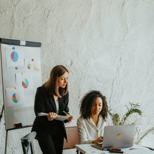 Two businesswomen analyzing graphs on a whiteboard during a meeting.